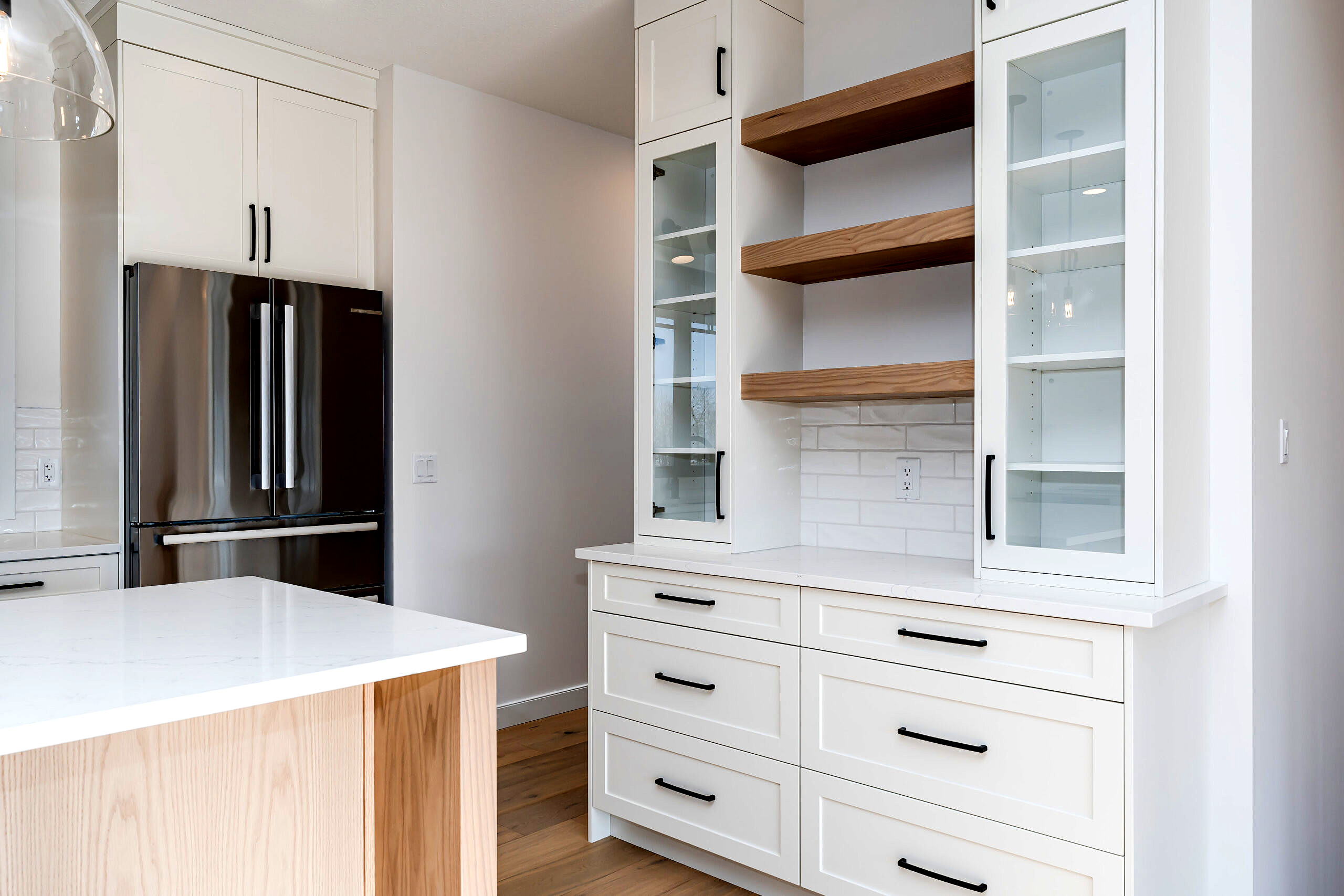 White kitchen with light-stained oak island and floating shelves.